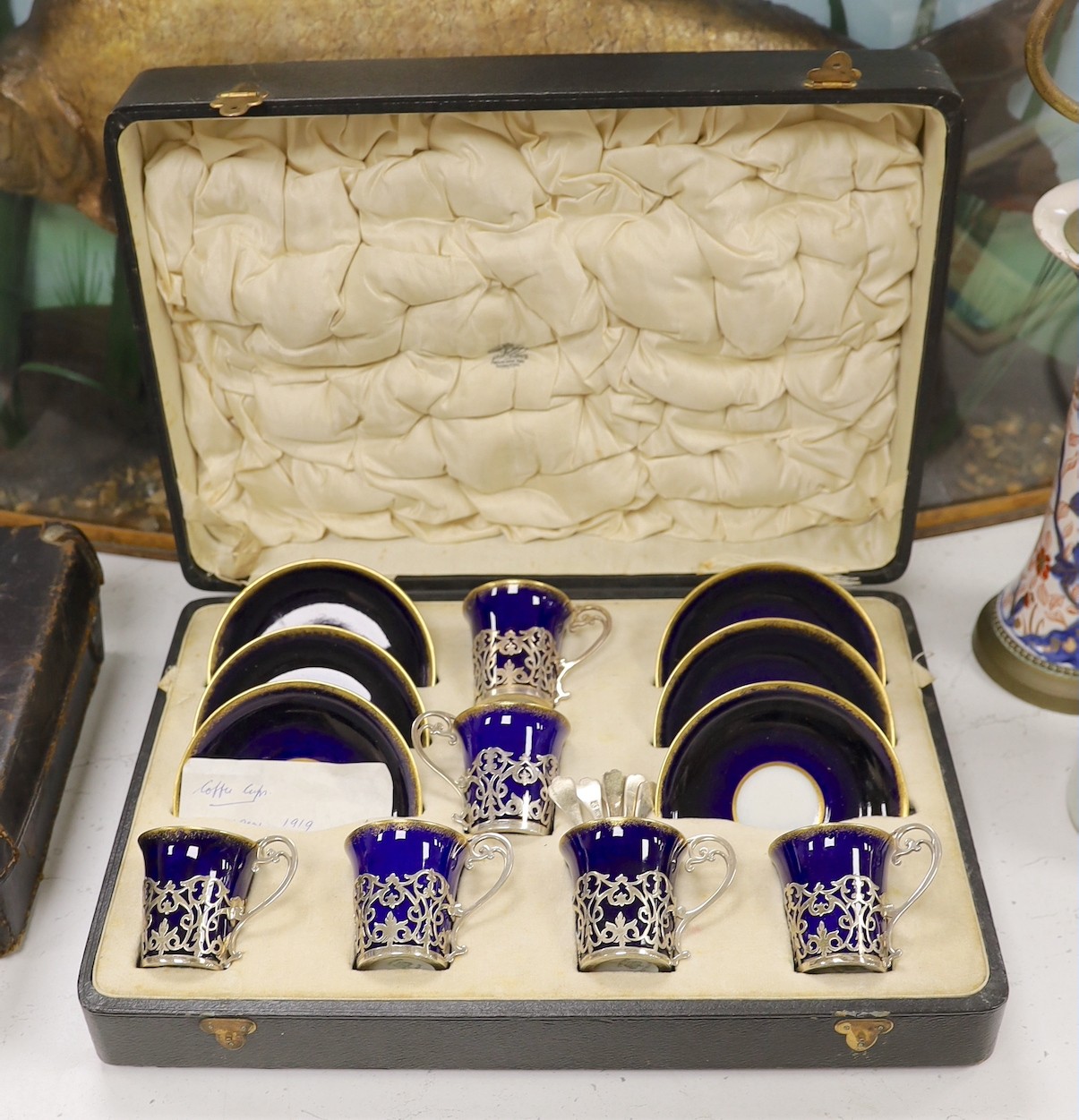 A set of six blue and gilt edged coffee cups and saucers, the cups with pierced silver holders, London, 1919, together with a set of 6 coffee spoons, triffid end terminals, Sheffield, 1925, cased